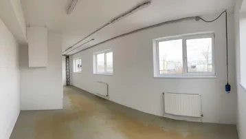 Heller, leerer Raum mit weißen Wänden, mehreren Fenstern und Heizkörpern, ideal für Büro oder Gewerbe.