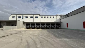 Außenansicht eines modernen Industriegebäudes mit mehreren Laderampen und großem Vorplatz.