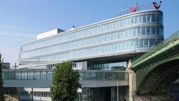 Modernes Bürogebäude mit geschwungener Glasfassade und markantem TUI-Logo, gelegen an einer Brücke.
