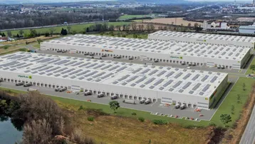 Luftaufnahme eines modernen Logistikparks mit mehreren Lagerhallen, ausgestattet mit Photovoltaikanlagen auf den Dächern.
