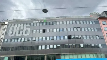 Moderne Bürogebäude-Fassade mit großen Fenstern und Firmenlogos unter bewölktem Himmel.