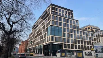 Modernes Bürogebäude mit vielen Fenstern und dunklen Rahmen an einer belebten Straße in der Stadt.