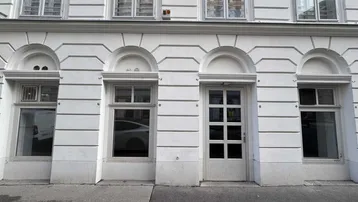 Nahaufnahme der weiß gestrichenen Fassade eines Altbaus mit Fenstern und einer Eingangstür im Erdgeschoss.