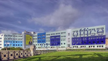 Großes Bürogebäude mit moderner Fassade in Blau- und Türkistönen und grüner Rasenfläche davor.