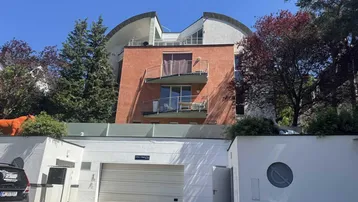 Modernes Gebäude mit geschwungener Architektur, Balkonen und einer Tiefgarageneinfahrt.