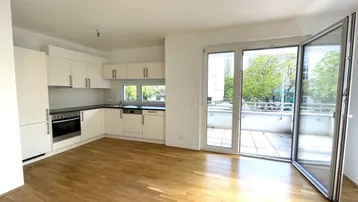 Heller offener Wohnbereich mit integrierter Küche, Parkettboden und Zugang zu einem großen Balkon.