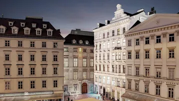 Abendliche Ansicht eines historischen Stadtplatzes mit beleuchteten Gebäuden und Geschäften.