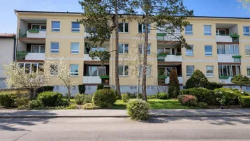 Mehrfamilienhaus mit gelber Fassade, Balkonen und gepflegter Grünanlage im Vordergrund.