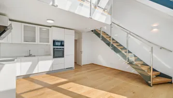 Helles, offenes Wohnzimmer mit integrierter Küche, Holzparkett und moderner Treppe zu einer Galerie.