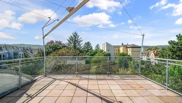 Geräumige Dachterrasse mit Fliesenboden, Glasgeländer und weitem Blick ins Grüne.