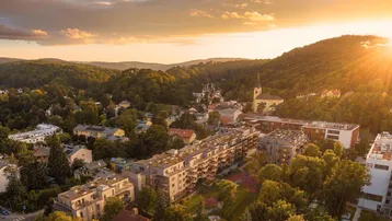 Luftaufnahme eines modernen Wohnkomplexes in grüner Hügellandschaft bei Sonnenuntergang.