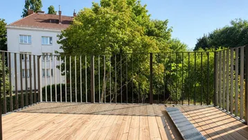 Geräumiger Balkon mit Holzboden und modernem Geländer, bietet einen schönen Blick ins Grüne.