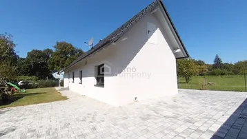 Modernes Einfamilienhaus mit weißer Fassade, gepflasterter Auffahrt und großem Gartenbereich.