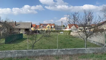 Grünes Grundstück mit Zaun und Blick auf umliegende Häuser unter blauem Himmel.