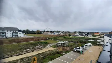 Weitläufige Außenansicht mit Neubauten, Parkplätzen und unbebautem Land unter bewölktem Himmel.