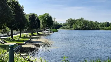 Idyllischer See mit grünen Ufern und Bäumen unter strahlend blauem Himmel.