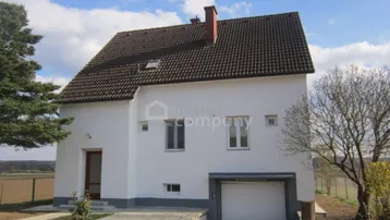 Weißes Einfamilienhaus mit Satteldach, integrierter Garage und weitem Blick über die Felder.