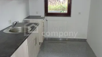 Funktionale Küche mit hellen Holzschränken, dunkler Arbeitsplatte und Fenster mit Blick ins Grüne.