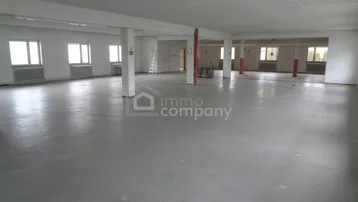 Großer, leerer Innenraum mit Betonboden und mehreren Fenstern, bereit für den Ausbau.