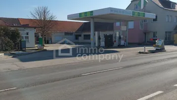 Eine Tankstelle mit angrenzenden Gebäuden und einer Straße unter blauem Himmel an einem sonnigen Tag.
