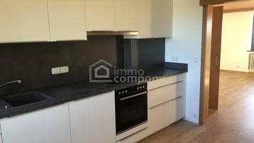 Moderne Einbauküche mit weißen Schränken, dunkler Arbeitsplatte und integriertem Backofen.