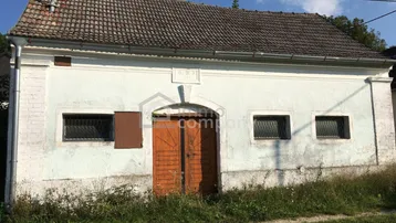 Altes, einfaches Gebäude mit weiß getünchter Fassade, Holztüren und vergitterten Fenstern unter einem Ziegeldach.