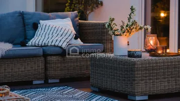 Gemütliche Terrasse mit Rattanmöbeln, Kissen und stimmungsvoller Beleuchtung am Abend.