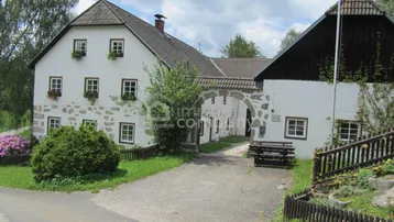 Traditionelles Landhaus mit weißer Fassade, Holzbalken und gepflegtem Vorgarten unter blauem Himmel.