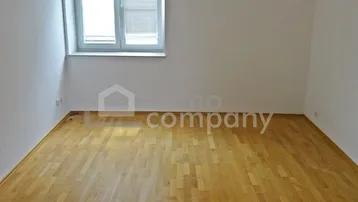 Helles Zimmer mit Parkettboden und einem Fenster, das viel Tageslicht hereinlässt.