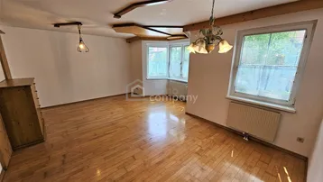 Geräumiges Wohnzimmer mit Holzboden, sichtbaren Deckenbalken und mehreren Fenstern für viel Tageslicht.