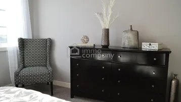 Helles Schlafzimmer mit einem eleganten dunklen Sideboard und einem gemusterten Sessel.
