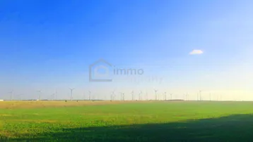 Weite grüne Landschaft unter blauem Himmel mit zahlreichen Windkraftanlagen am Horizont, die Energie erzeugen.