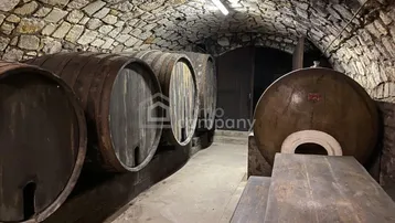 Historischer Weinkeller mit Steingewölbe, großen Holzfässern und rustikalem Holztisch.