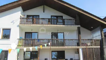 Traditionelle Hausfassade mit zwei Balkonen, Holzelementen und einem Satteldach in sonniger Lage.