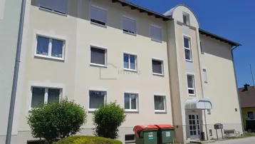 Mehrfamilienhaus mit heller Fassade, Rollläden an den Fenstern und einem Eingangsbereich.