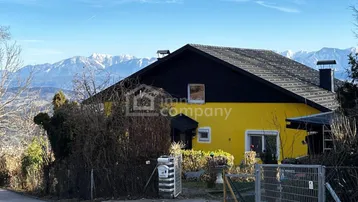 Gelbes Haus mit schwarzem Dach und Bergblick in sonniger Lage.