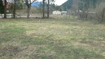 Unbebautes Grundstück mit spärlichem Gras, umgeben von Bäumen und mit Blick auf bewaldete Berge.