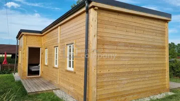 Kleines Holzhaus mit einfacher Architektur und weiß gerahmten Fenstern unter blauem Himmel.