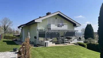 Rückansicht des Hauses mit Balkon, überdachter Terrasse und weitläufigem Rasen.