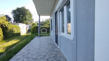 Gedeckter Terrassenbereich mit Fliesenboden entlang der Hausfassade und Grünflächen.
