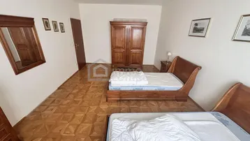 Schlafzimmer mit zwei Betten, Holzschrank und Parkettboden in Fischgrätmuster.
