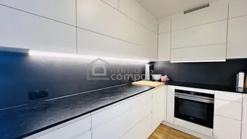 Moderne Küche mit weißen Schränken, dunkler Arbeitsplatte und integriertem Backofen.