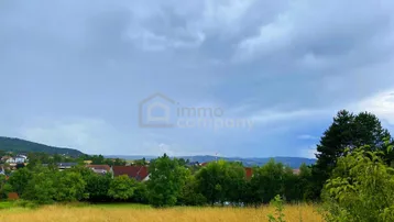 Weitläufiger Blick über eine ländliche Landschaft mit Häusern, Bäumen und bewölktem Himmel.