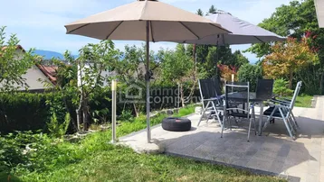 Gepflasterte Terrasse mit Gartenmöbeln, Sonnenschirmen und angrenzender Rasenfläche.