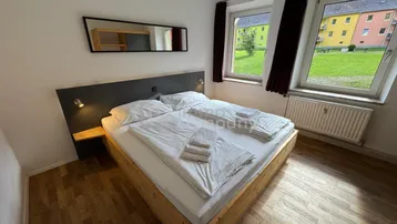 Gemütliches Schlafzimmer mit Doppelbett und Blick ins Grüne durch große Fenster.