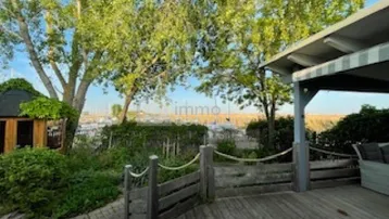Geräumige Holzterrasse mit Blick auf den Hafen und üppige Bäume, ideal zum Entspannen im Freien.
