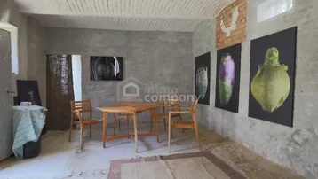 Rustikaler Innenraum mit unverputzten Wänden, Holztisch und Kunstwerken an der Wand.