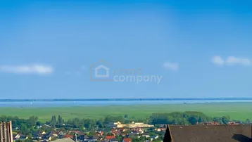 Weitläufiger Blick über eine Küstenstadt, grüne Felder und das Meer unter blauem Himmel.