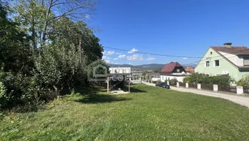 Weitläufiges Grundstück mit grüner Wiese, Bäumen und Blick auf umliegende Häuser und Hügel.