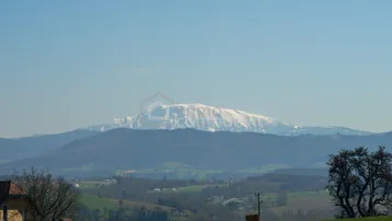 Weitblick auf eine schneebedeckte Bergkette unter klarem Himmel, umgeben von grünen Hügeln.
